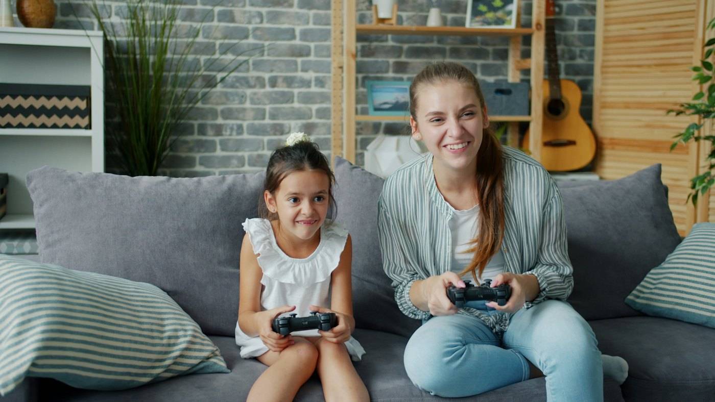 A mother and a small daughter playing a video game on the sofa